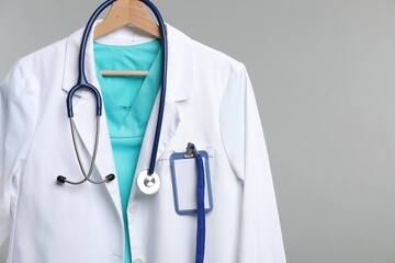 Doctor's coat with stethoscope and badge on hanger against grey background