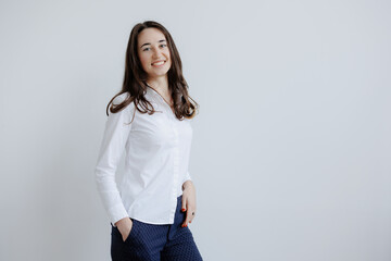 Young woman standing confidently against a plain background in a white shirt and dark pants during...