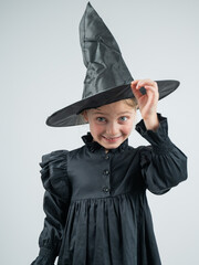 Fototapeta premium Portrait of a little Caucasian girl in a witch costume on a white background. Vertical photo. 