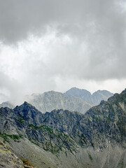 Dark grey mountain peaks with more mountain beaks in the background and low grey clouds on top, High Tatra mountains, Slovakia