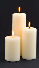 Three burning ivory pillar candles on black background, varying sizes
