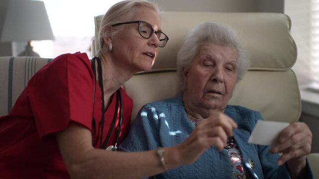A caregiver engages with a senior resident at a memory care facility, focusing on a card during an afternoon activity. Both are involved in a meaningful exchange.