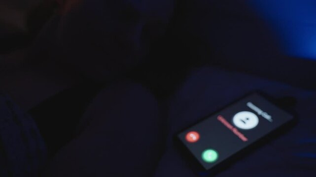 Incoming Call from Unknown Number Appears on Smartphone Screen Resting on Bed in Dark Room with Blue Light, Close-Up Angle, Late Night Disturbance Concept