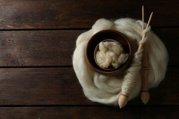 Soft white wool and spindles on wooden table, top view. Space for text