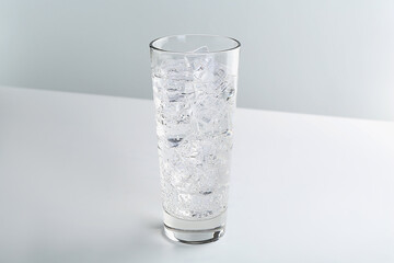 Refreshing soda water with ice cubes in glass on white table against light background