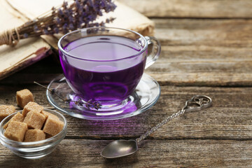 Aromatic lavender tea in glass cup, brown sugar, book, spoon and bunch of dry flowers on wooden...