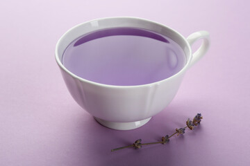Aromatic lavender tea in cup and dry flowers on lilac background, closeup
