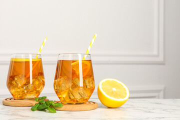 Refreshing iced tea with slices of lemon, mint and drinking straws on white marble table, closeup....