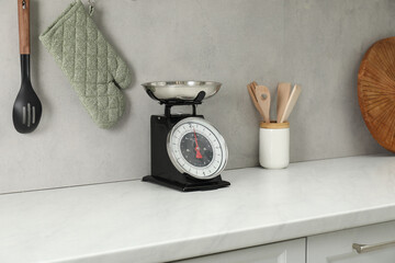 Retro mechanical kitchen scale on white marble countertop and other utensils indoors