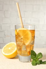 Refreshing iced tea with drinking straw, mint and slices of lemon on light textured table against grey background, closeup