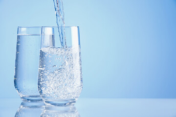 Pouring refreshing soda water into glasses on light blue background, closeup. Space for text