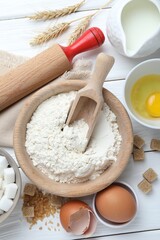 Rolling pin and ingredients for dough on white wooden table, flat lay