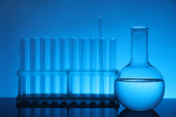 Laboratory glassware with liquid on mirror surface against light blue background