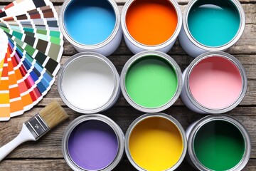 Cans of bright paints, brush and color palettes on wooden table, flat lay