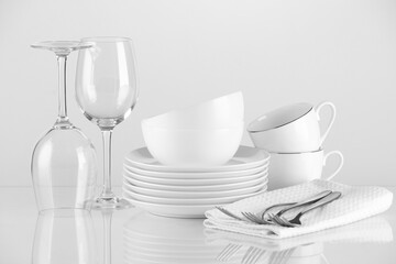 Different clean dishware and cutlery on light background