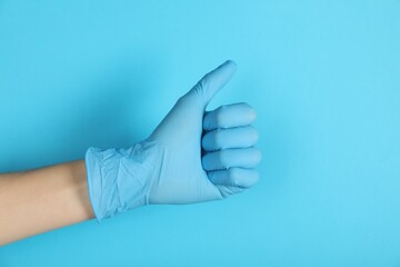 Doctor in medical glove showing thumbs up on light blue background, closeup