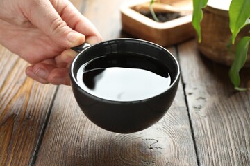 Woman with freshly brewed tea at wooden table, closeup