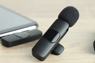 Lavalier microphone and smartphone with wireless receiver on wooden table, closeup