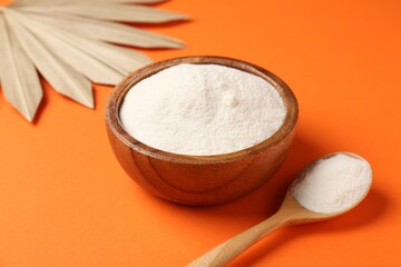 Collagen powder in bowl, spoon and dry palm leaf on orange background, closeup