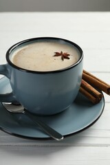 Aromatic Masala tea in cup, cinnamon and anise star on white wooden table, closeup