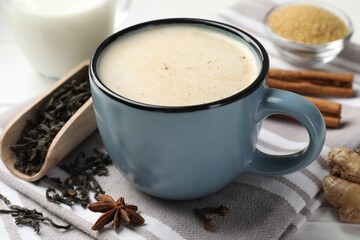 Aromatic Masala tea in cup, spices, dry leaves, milk and brown sugar on table, closeup