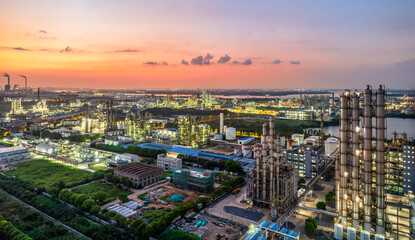 Obraz premium Aerial view of illuminated oil refinery at dusk with industrial zone waterfront and colorful sky background