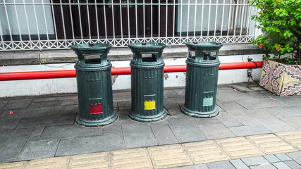 Three trash bins on the sidewalk. Having coloured markings on the bottom according to the type of waste accommodated.