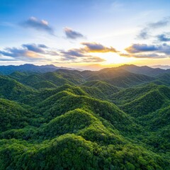 Fototapeta premium Sunrise over lush green rolling hills and mountains. Golden hour light bathes the landscape in warm tones. Clouds fill the sky above.