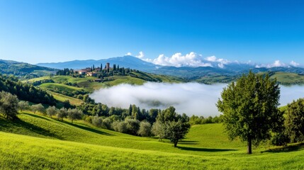 Obraz premium Morning mist rolls through a lush green valley, revealing a quaint village nestled on a hillside under a vibrant blue sky. Trees dot the landscape, creating a picturesque scene.