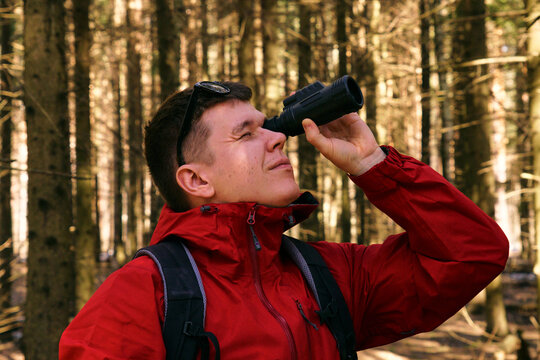 A man looks through monocular binoculars in the woods in nature. Search for new opportunities