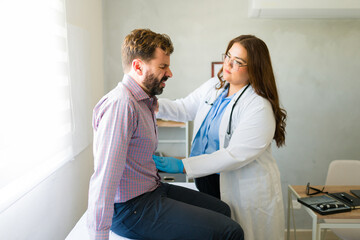 Doctor wearing gloves palpating the abdomen of a male patient experiencing pain during medical...