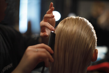 Fototapeta premium Close-up of a hairstylist combing and shaping straight blonde hair. Salon beauty treatment and expert hair care in progress