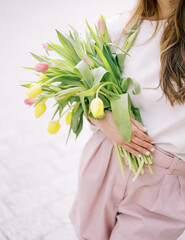 Naklejka premium Girl stands holding a bouquet of bright flowers to her stomach. Cropped. Faceless