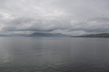 Fototapeta premium view of mountains that line the river Clyde from Dunnon to Gourock ferry in West coast Scotland. slight mist and cloud give mystical feel to stunning dramatic landscape scenery on cloudy day