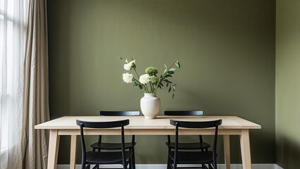 Serene simplicity: a light-filled dining space adorned with delicate white flowers in a minimalist vase against a calming olive green wall.