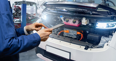 Serviceman with digital tablet next to electric van with open hood. Electric vehicles maintenance.