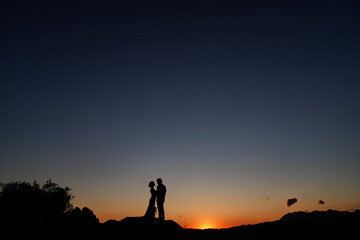 Silhouettes of bride and groom standing on the mountain at sunset