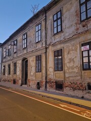 Old damaged facade of a house near the road with a tree on the roof