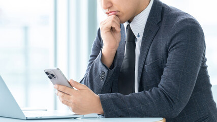 スマートフォンを見て考える男性ビジネスマン