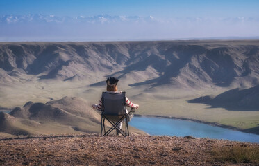 A woman sits on a tourist chair admiring the beautiful view of the mountains and the Ili River...
