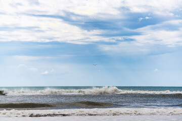 Waves crash onto the shore beneath a vast sky with scattered clouds.