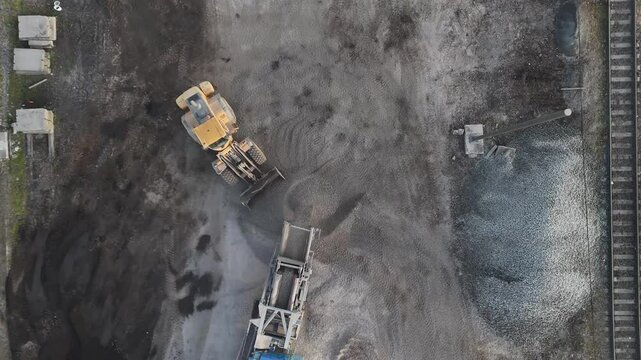A drone captures an excavator with a bucket loading construction waste into a vibrator for sorting. Industrial worksite in action!