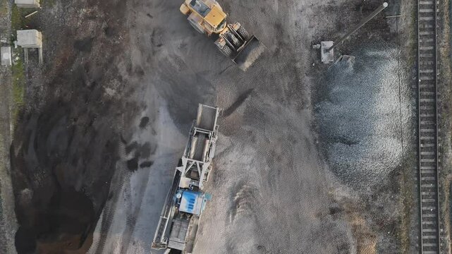 A drone captures an excavator with a bucket loading construction waste into a vibrator for sorting. Industrial worksite in action!