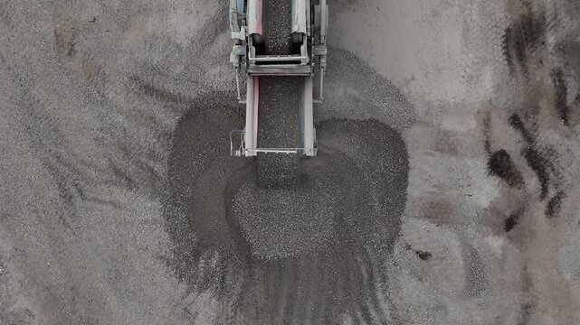 A drone captures an excavator with a bucket loading construction waste into a vibrator for sorting. Industrial worksite in action!