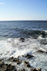 vista del mar desde la costa en dia de verano luminoso, cielo y mar azules olas en accion moderada ocasionan espuma blanca.
