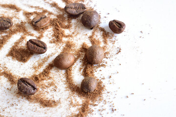 Roasted and ground coffee beans lie chaotically on a white background.