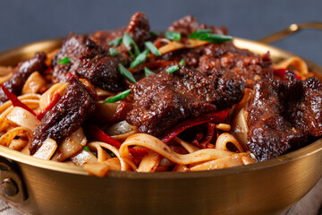Udon noodles with beef in Mongolian style, with green onions and vegetables, homemade, on a dark background,