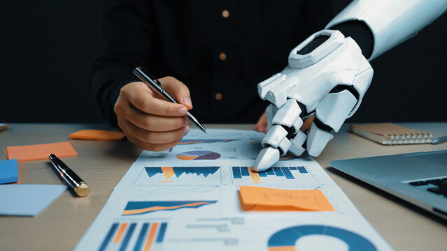 A unique scene depicting a robotic hand assisting a human in analyzing business charts and graphs, showcasing the future of technology and productivity in the workplace.Noogenesis