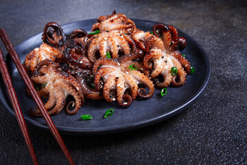 Grilled baby octopus, served with chopsticks, on a black plate, homemade, no people,