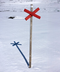 A cross-country trail sign stands firm in a vast snowy landscape, casting a crisp shadow in the winter sun. A symbol of direction, solitude, and the beauty of Nordic wilderness.